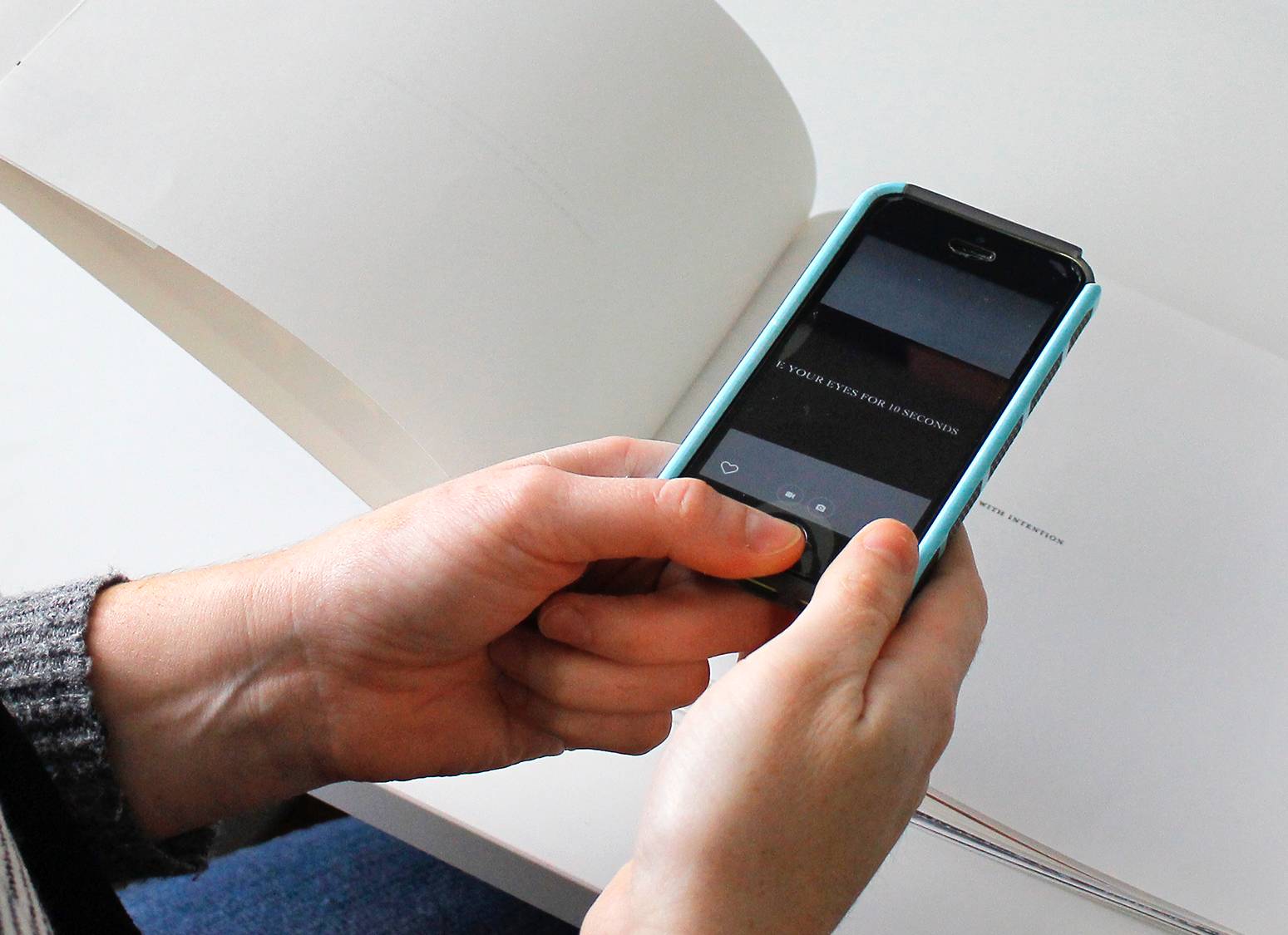 Image of person holding a mobile smart phone and pointing its camera to one of the book pages and revealing bonus content through Augmented Reality.